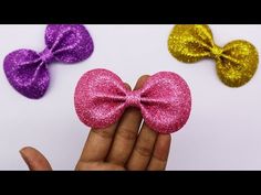 someone is holding three small bows in their hand, one pink and one purple with gold sequins