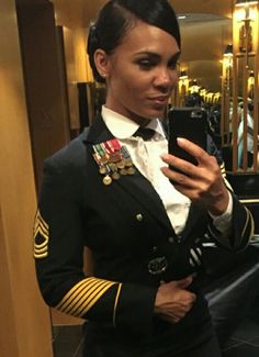 a woman in uniform is looking at her cell phone and taking a selfie with the mirror behind her