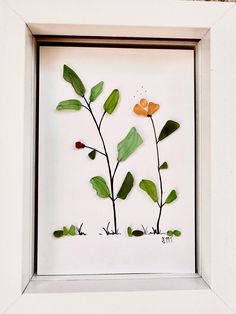 a white frame with some green and orange flowers in the bottom right hand corner is a shadow box