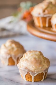 three muffins with frosting on top sitting on a marble table next to other muffins