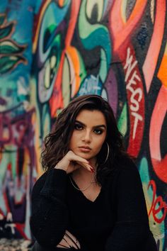 a woman sitting in front of a wall with graffiti on it and her hand under her chin