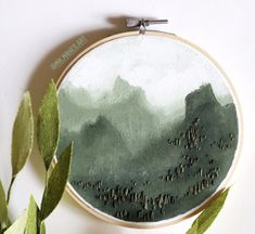 a cross stitch pattern with mountains in the background and leaves on the table next to it