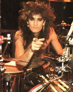 a man with long hair sitting in front of a drum kit