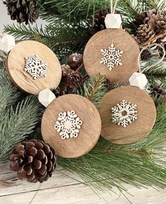 three wooden ornaments with snowflakes on them and pine cones in the foreground