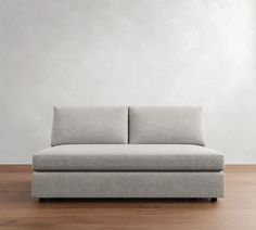 a gray couch sitting on top of a wooden floor next to a white wall in an empty room