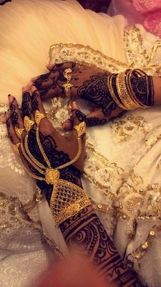 a woman with henna on her hands laying down next to a white dress and gold jewelry