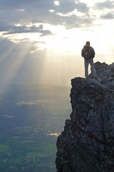 a man standing on the edge of a cliff looking out over a valley and mountains