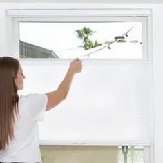 a woman standing in front of a window with roller shades on it's windowsill