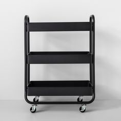 a three tiered shelf on wheels against a white wall with no one in it