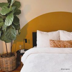 a bed with white sheets and pillows next to a potted plant in a basket