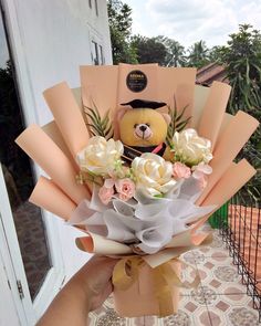 a person holding a bouquet of flowers with a teddy bear in the middle and an envelope behind them