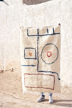 a person standing in front of a white wall holding a blanket with an abstract design on it