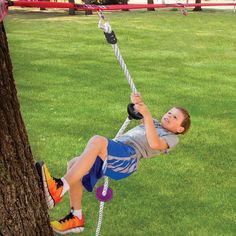 a young boy is swinging on a rope in the park while holding onto a tree