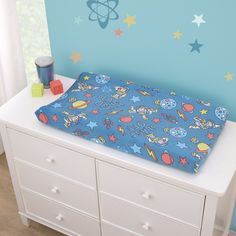 a baby's crib with space themed sheets and toys on the top drawer