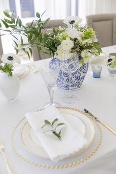 a table set with white and blue plates, silverware and flowers in vases