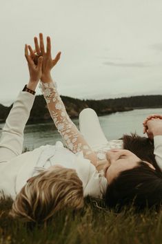 two people laying on the grass with their hands in the air