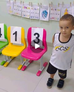 a little boy standing in front of three colorful chairs with numbers on each one side