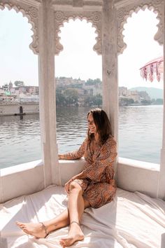 a woman sitting on top of a bed in front of a window next to water