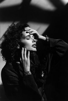 a black and white photo of a woman with her hands on her face, looking off to the side