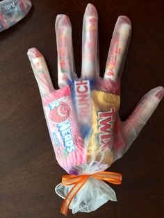 a hand made out of candy wrapper sitting on top of a wooden table next to an orange ribbon