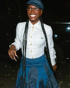 a woman with long braids wearing a blue skirt and hat smiles at the camera