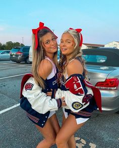 two cheerleaders are posing for the camera in front of a car and parking lot