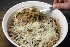 a person is holding a spoon in a bowl of pasta and meat with parmesan cheese on top