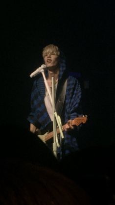 a man holding a guitar while standing in front of a microphone on top of a stage