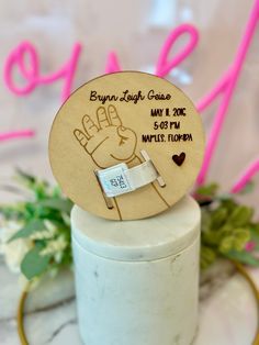 a close up of a small wooden sign on top of a white container with flowers in the background