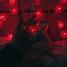 a person is holding a wine glass in front of red hearts on the wall behind them