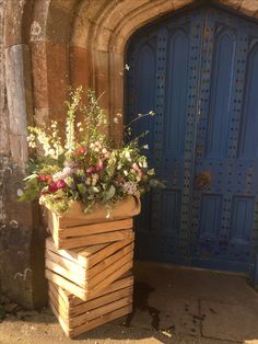 a wooden planter with flowers in front of a blue door