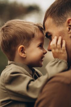 a man holding a little boy in his arms while he looks at the other side