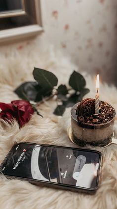 a cell phone sitting on top of a white fur covered floor next to a candle