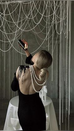 a woman in a black dress holding a cell phone up to her ear and wearing pearls