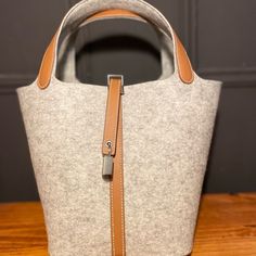 The Hermes Picotin In Wool, In The Elegant Color Gris, Is A Sophisticated And Timeless Accessory. This Bag, Renowned For Its Minimalist Design And Superior Craftsmanship, Is Crafted From Premium Wool, Offering A Unique And Luxurious Texture. The Gris Color Provides A Versatile And Chic Aesthetic, Perfect For Any Wardrobe. This Particular Picotin Is In Excellent Condition, Showcasing Minimal To No Signs Of Wear, Ensuring Its Status As A Cherished Piece For Years To Come. Comes With Dustbag, Lock And Key Condition: Excellent Material: Wool And Swift Leather Hermes Picotin Size, Hermes 24/24 Bag, Lock And Key, Timeless Accessories, Hermes Bags, Minimalist Design, Dust Bag, Bag Lady, Wool