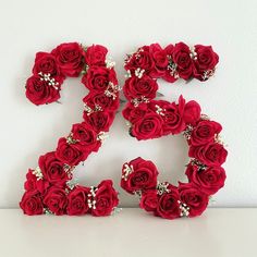 the number twenty five made out of red roses and pearls is displayed in front of a white wall