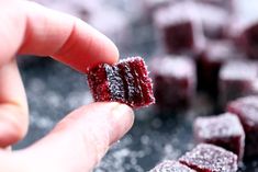 a hand holding a piece of red velvet cake with sugar on the top and other pieces in the background