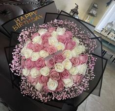 a bouquet of pink and white roses sitting on top of a black table next to a happy birthday card