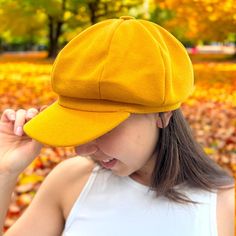 a woman wearing a yellow hat in the fall with leaves on the ground behind her