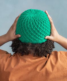 a person wearing a green crochet hat with their hands on the back of their head