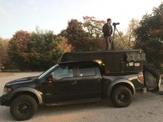 a man standing on the back of a black truck with a camera in its bed