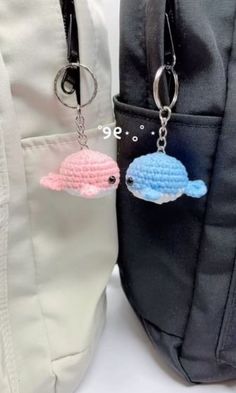 two crocheted fish keychains are hanging from a backpack strap in front of another bag