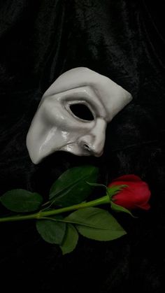 a white mask sitting next to a red rose