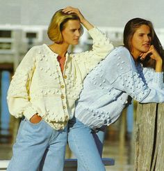 two women standing next to each other wearing sweaters and jeans, one in blue