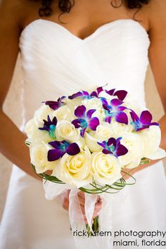 a bride holding a bouquet of white roses and purple orchids in her wedding dress