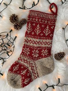 a red and white knitted christmas stocking next to pine cones on a fur rug