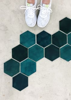 a pair of white tennis shoes sitting on top of a tiled floor next to green hexagonal tiles