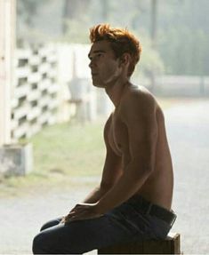 a shirtless young man sitting on top of a wooden bench next to a fence