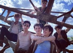 four young men sitting on top of a wooden structure with their arms around each other