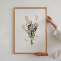 a person holding up a framed painting with pink tulips in the center and white ribbon around it